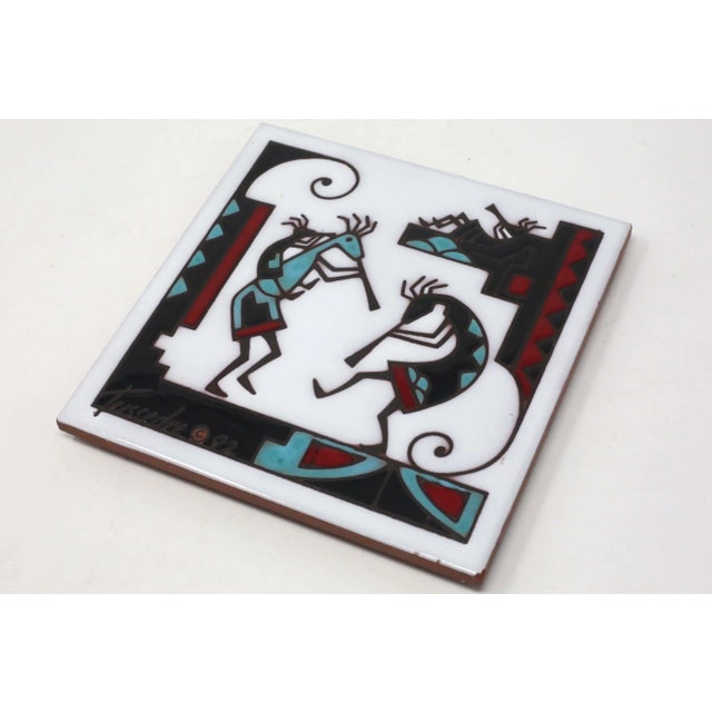 A 1992 handmade ceramic tile, decorated with a 90's tribal design depicting musicians. It has a hole for hanging, and a...