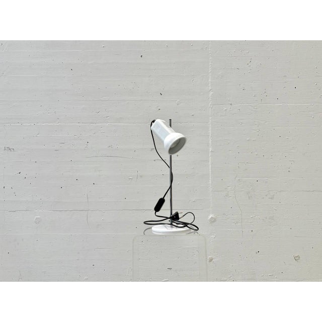 A distinctive 1970s table lamp with a clean, space-age aesthetic and functional industrial charm. The cylindrical lamp...