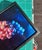 This oil painting on birch panel depicts a cluster of grapes, rendered in rich hues of purple and blue against a dark...
