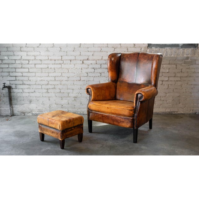 Vintage distressed cognac leather wingback chair and ottoman set, circa 1970s. Beautifully distressed cognac leather with...