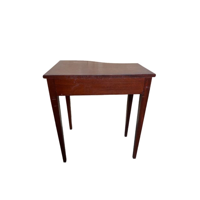 A Hepplewhite Style Mahogany Side Table that is burnt umber. This table has a curved top and one drawer and is from the...