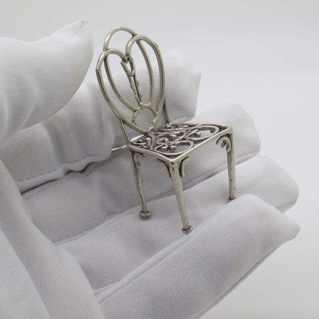 This vintage silver decorative object depicts an elegant chair figurine miniature, crafted as a dollhouse centerpiece,...