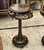 A refined French Neoclassical side table crafted with a rich dark wood finish, a glass-inset tabletop, and delicate gold...