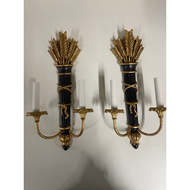 This is a pair of mid-century Italian made decorative two-light electrical wall sconces with black lacquered gilt wood...