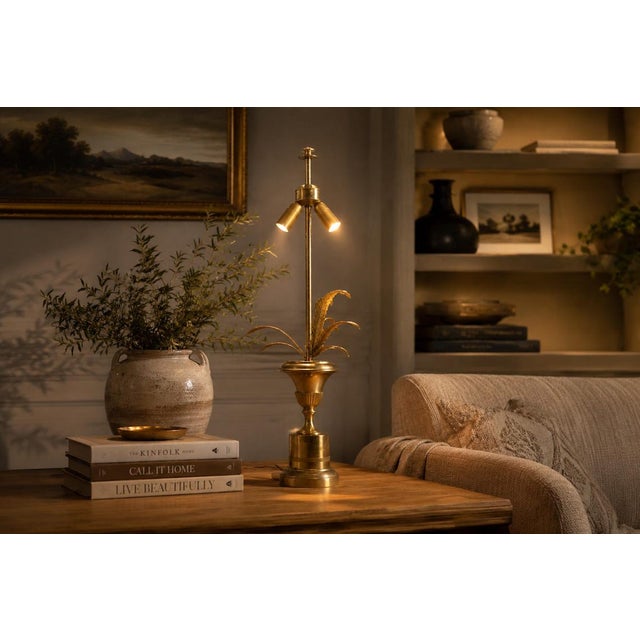 A tall and elegant brass table lamp featuring the iconic hollywood regency palm leaf motif, here presented in a slightly...
