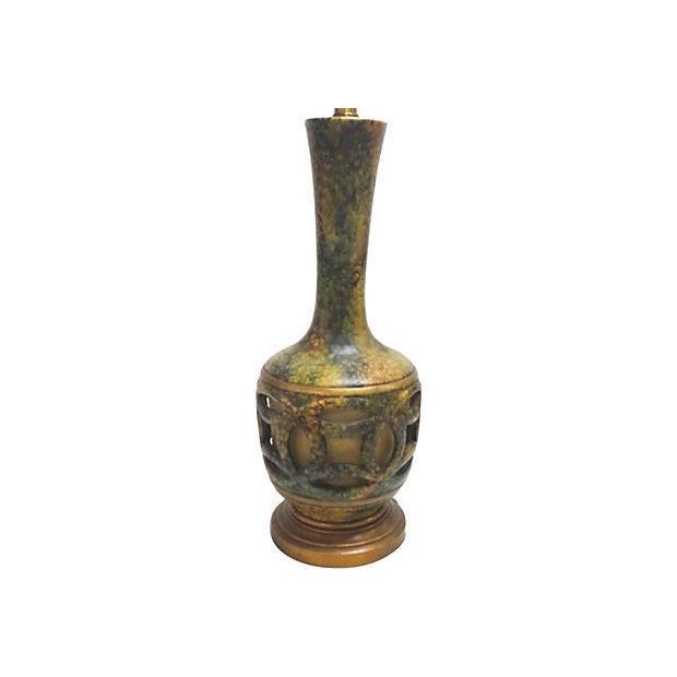 A 60s era tall art pottery lamp in ceramic in shades of greens and browns. This large scale lamp has cut outs in the base...