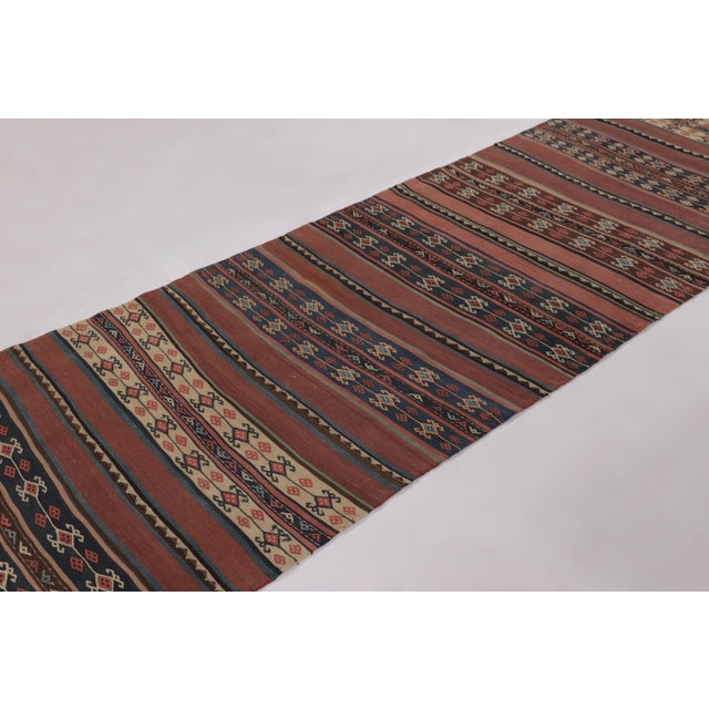 Made with handwoven wool circa 1950-1960, this 3x13 vintage Persian Kilim runner enjoys complex horizontal band and tribal...