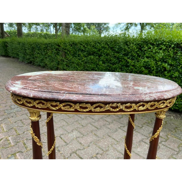 A refined 1970 French Louis XVI–style side table, handcrafted from solid mahogany with a natural marble top and finely...