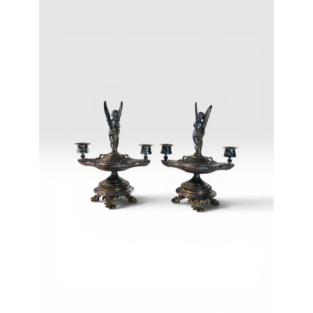 A beautifully detailed pair of antique Victorian silver-plated figural candlesticks featuring winged cherubs standing atop...