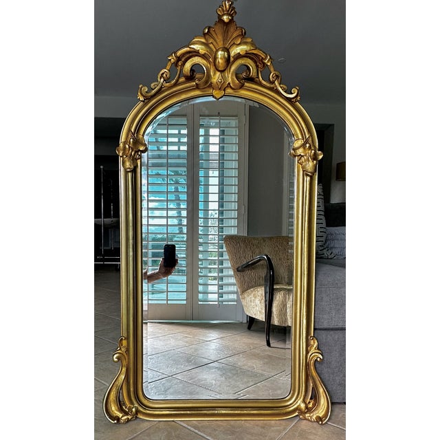 French Louis XV-style arched giltwood wall mirror. This striking piece beautifully captures the fluid asymmetry and...