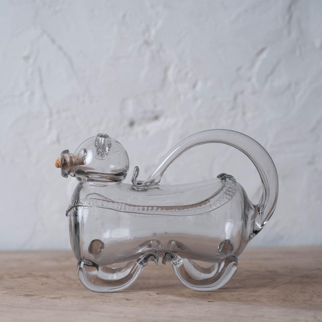 A vintage figural decanter crafted in clear hand-blown glass, designed as a playful dog with a cork stopper at the mouth...
