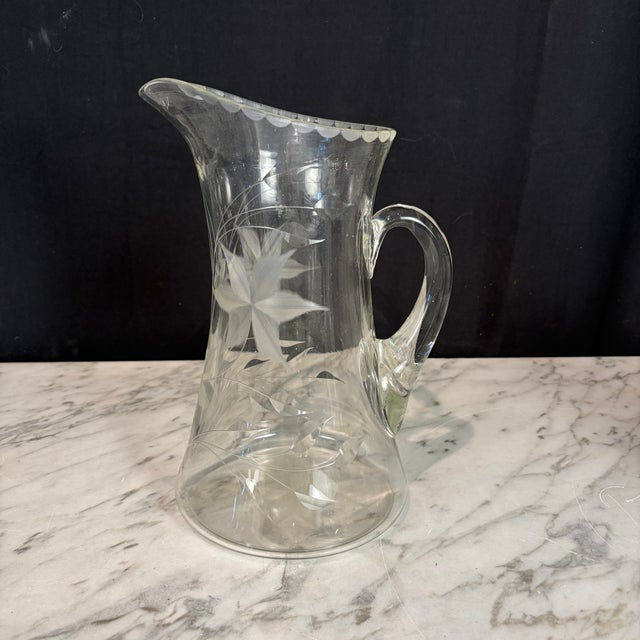 Elegant antique hand-blown clear glass pitcher featuring a finely wheel-etched floral and foliate motif with a delicately...