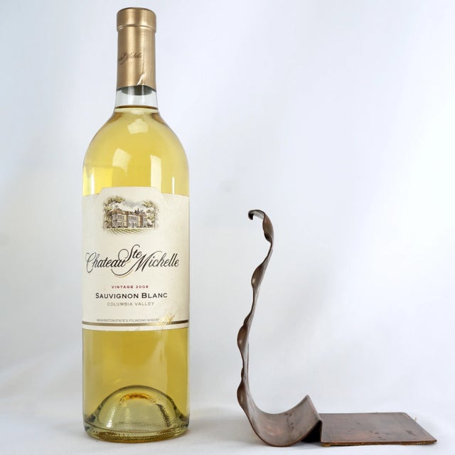 A bookend in the shape of a tropical leaf that has been formed from a thick sheet of copper. The base of the bookend is...