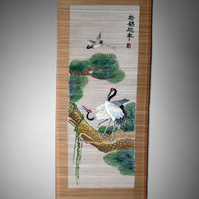 A beautiful Japanese bamboo blinds scroll featuring an elegant scene of cranes and pine trees, symbols of good fortune and...