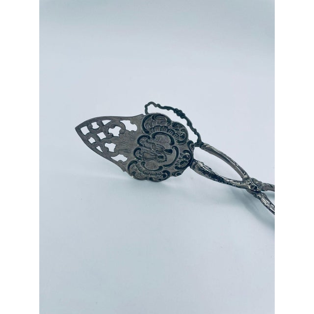 Vintage-style cake tongs from the 1970s, crafted from silver-colored metal. These scissor-shaped tongs are adorned with...