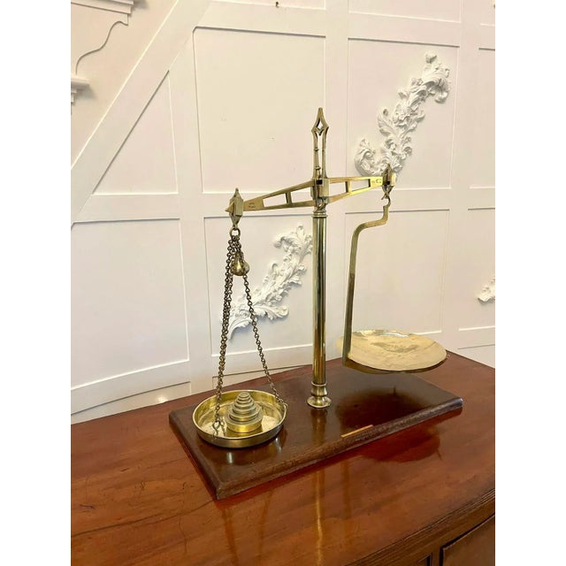 Pair of antique brass scales standing on a mahogany base. A brass centre column having a shaped arm to the left holding a...