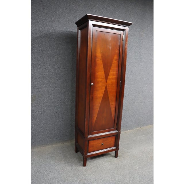 American Signature cherry linen press cabinet featuring a tall, narrow profile with geometric wood veneer detail,...