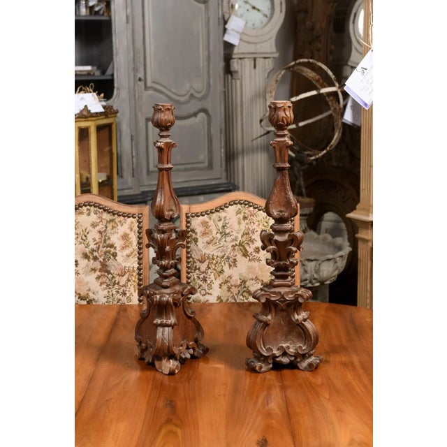 A pair of Italian Baroque period carved wooden candlesticks with acanthus leaves, volutes, carved scrolling feet and great...
