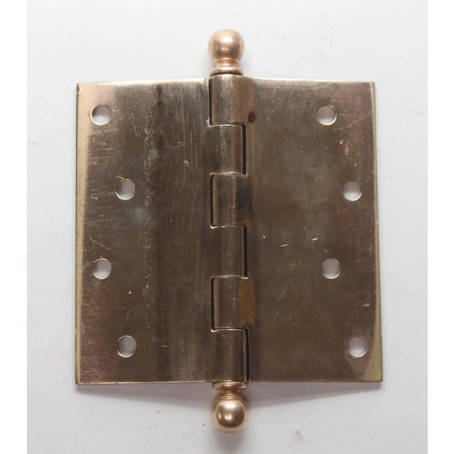 Antique brass door hinge with ball tips, six knuckles, and a staggered hole pattern. The original mounting screws are not...