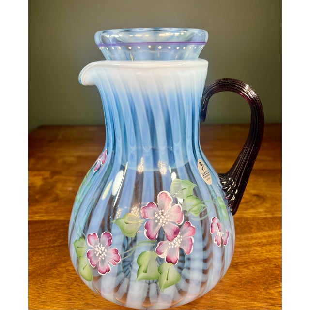 Signed Fenton 75th Anniversary guest set art glass pitcher. Light blue opalescent in color featuring a plum handle.