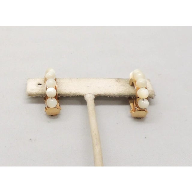 This is part of Chairish’s Costume Jewelry assortment. 1970s goldtone half hoop mother of pearl beaded clip earrings....