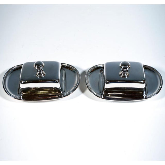 Two elegant, simple silver serving dishes with smooth sides – flat, oblong bowls with a recess for a glass top, and a...