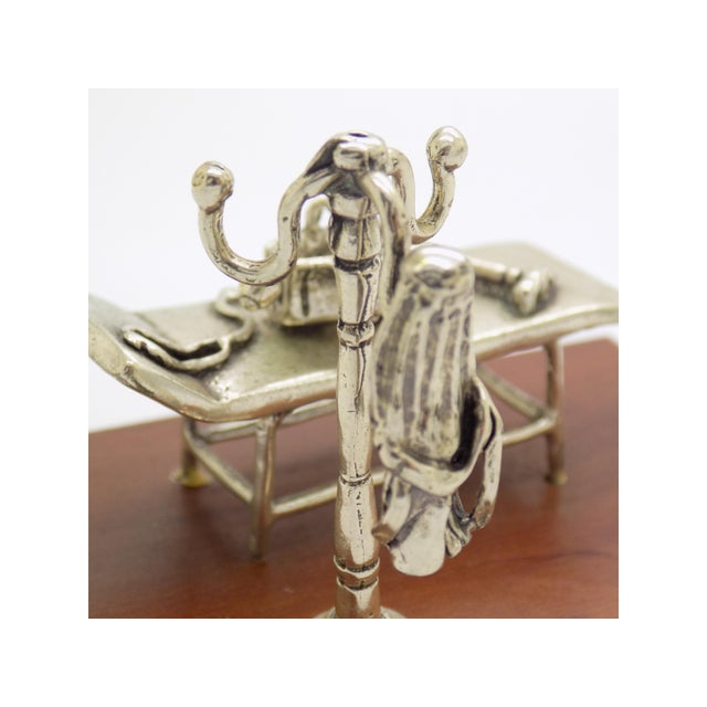 This vintage silver figurative diorama depicts a doctor's cabinet scene mounted on a wooden base, crafted as a medical...