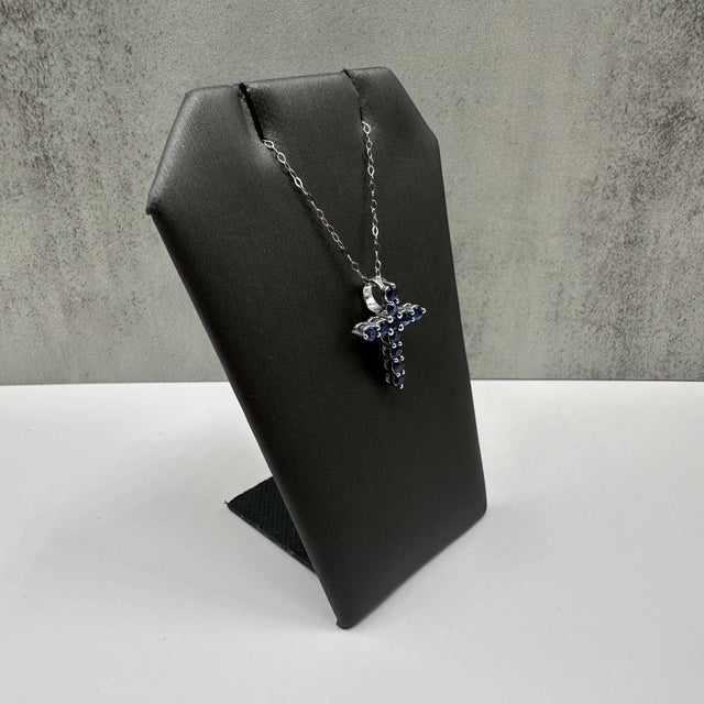 This beautiful blue sapphire cross necklace in 14kt white gold features 0.88 carats total weight of round blue sapphires...