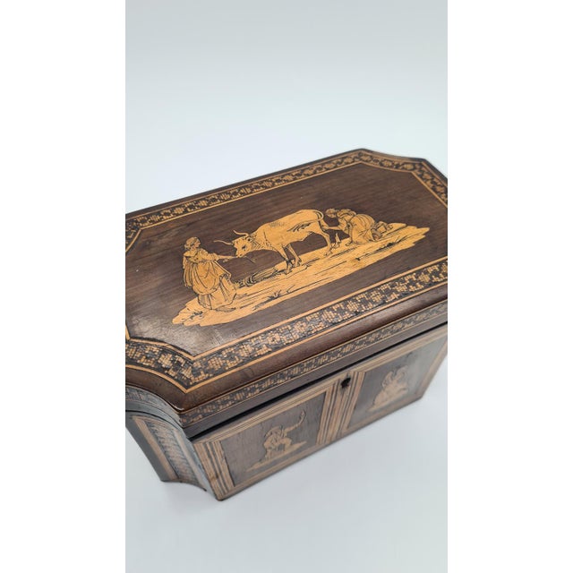 An original antique box/tea container, made of wood and richly decorated with figurative motifs (genre scenes) inlaid into...
