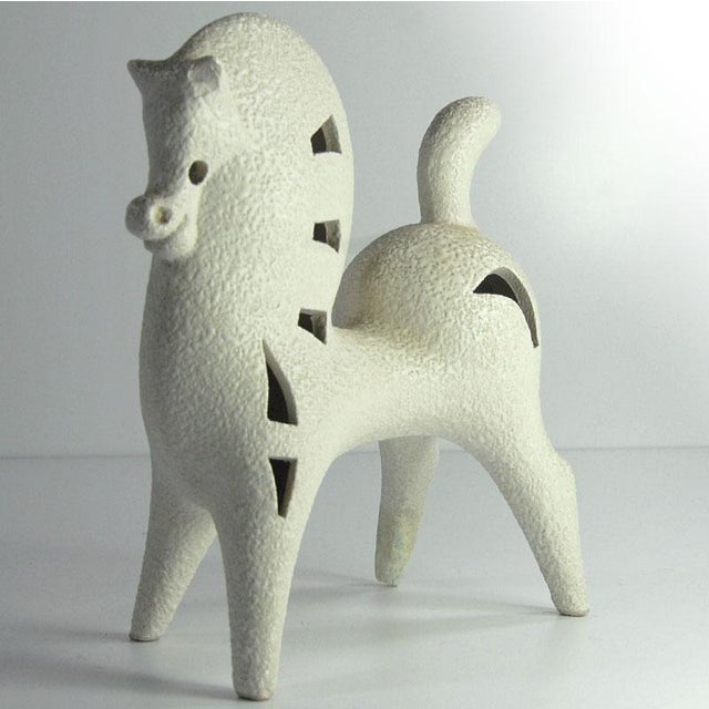 A decorative ceramic figurine of a highly stylized horse. Glazed in an off-white, slightly creamy glaze with an attractive...