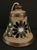 Beautiful handcrafted & hand painted Mexican Folk Art bell adorned with a blue flower and greenery against a specked brown...