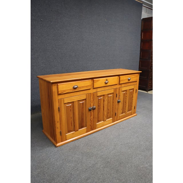 Pine sideboard featuring three drawers above three paneled cabinet doors, with a warm honey-colored finish and pronounced...
