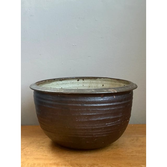 This vintage monumental rustic ceramic bowl is crafted from stoneware and finished in a rich brown glaze that softly...
