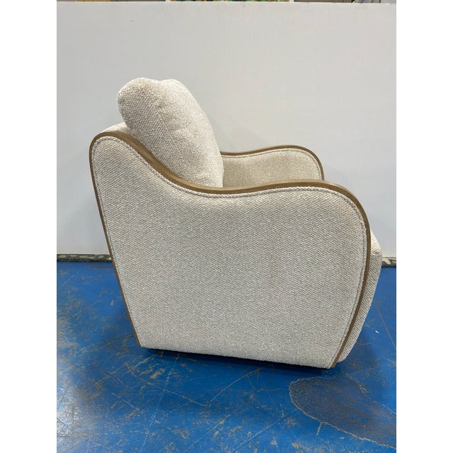Stylish Modern swivel chair with wood trim arms, upholstered with a nubby cream fabric. Showroom floor sample.