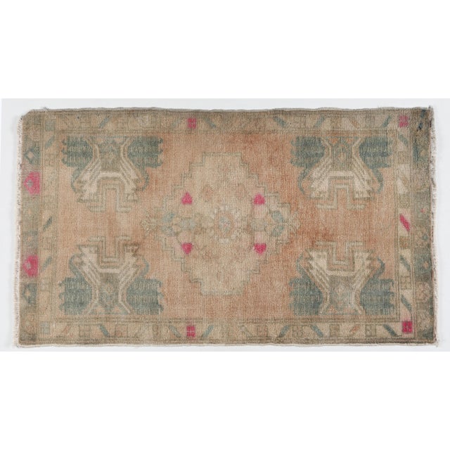 A vintage Turkish handwoven door mat rug featuring a bold geometric medallion and tribal motifs. Softly faded blush, sand,...