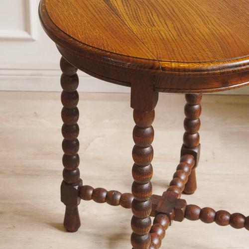 A historic round side table made of oak, circa 1900, with a turned base and cross-linked struts. Its compact height,...