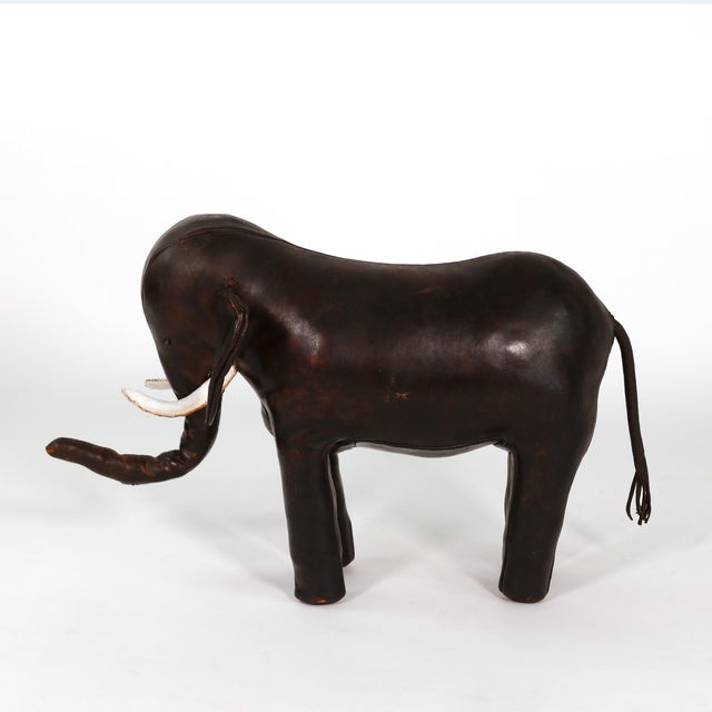 A standing elephant-form footstool in dark brown leather, the body assembled from shaped stitched panels with a hand-...