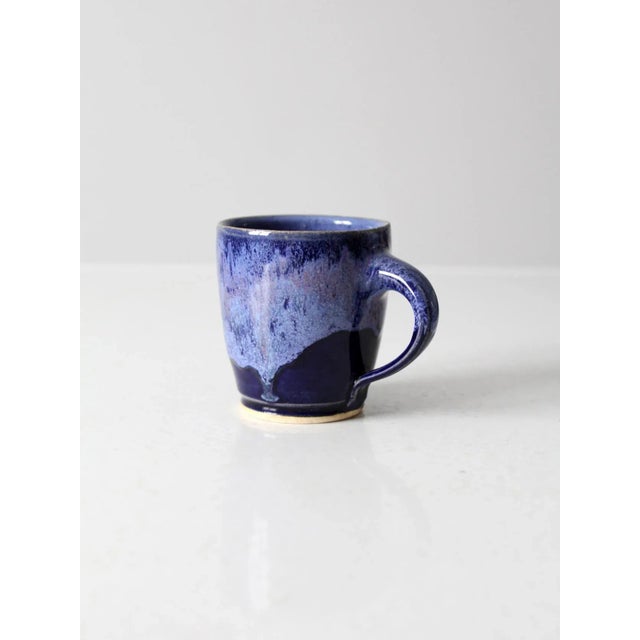 Handcrafted vintage studio pottery mug featuring a rich, expressive glaze in layered tones of blue and purple. The organic...
