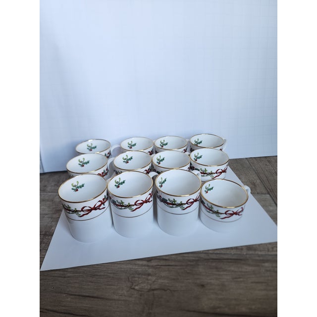 Eleven Holly Ribbon pattern christmas mugs and one shorter one. All together there are twelve cups.