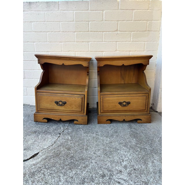 Pair of vintage American-style nightstands constructed from maple wood and features decorative carved details on the base....