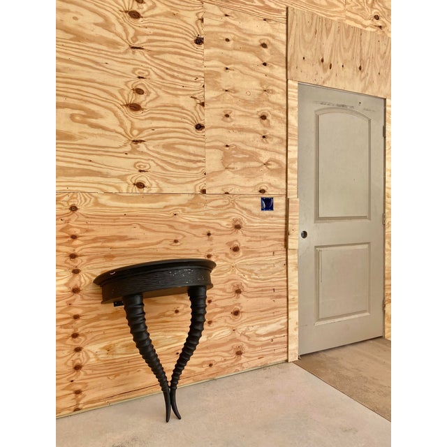 A unique, wall-mounted, demi-lune console table crafted in a dual-horn form, updated with a matte black surface that...