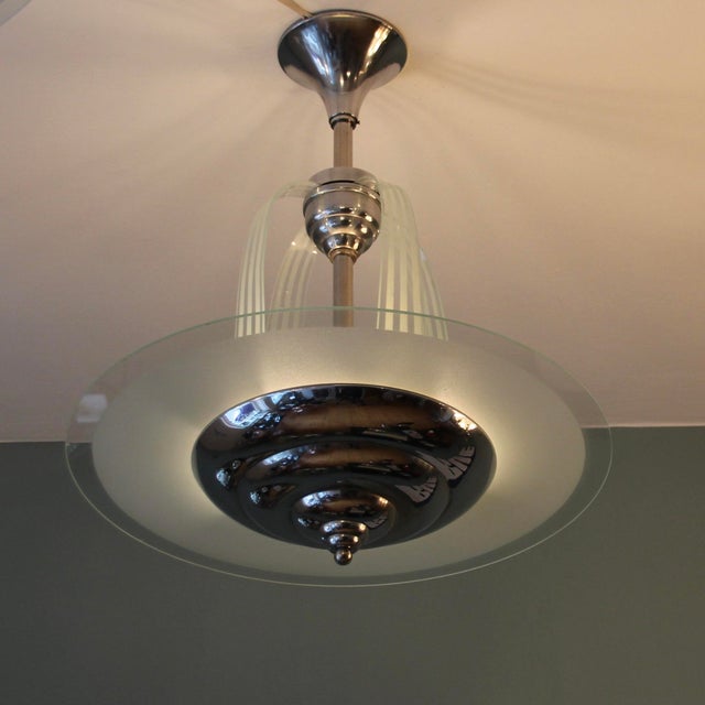 This round Art Deco chandelier, featuring four curved, thin glass strips reminiscent of a comet's tail or a waterfall, is...