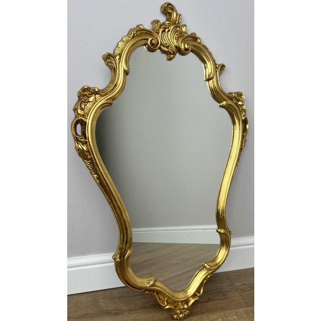 A stunning Vintage French style wall mirror featuring an elegant ornate gold-toned frame with flowing curves and...