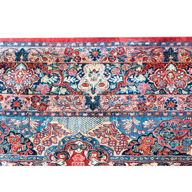 This exquisite 1930s Persian Kazvin rug features a vibrant red field adorned with an intricate floral medallion in shades...