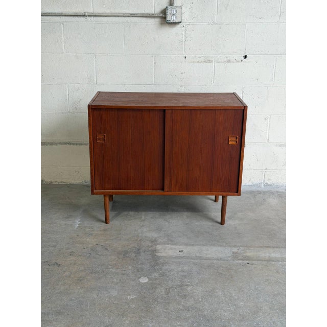 Vintage Danish modern teak cabinet featuring clean Scandinavian lines, tapered legs, and minimalist sliding doors with...