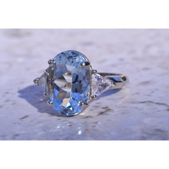 The Aubree: Lovely 14 karat white gold ring set with a 5.50 carat oval brilliant cut Aquamarine Beryl. On either side is a...