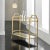 Modern Gilt Bar Cart with brass frame wrapped in textured gold with two shelves, tapered legs raised on brass casters. The...