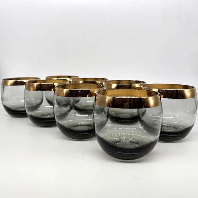 A refined set of eight mid-century smoky gray roly poly cocktail glasses with luminous gold rims. The rounded, low-profile...