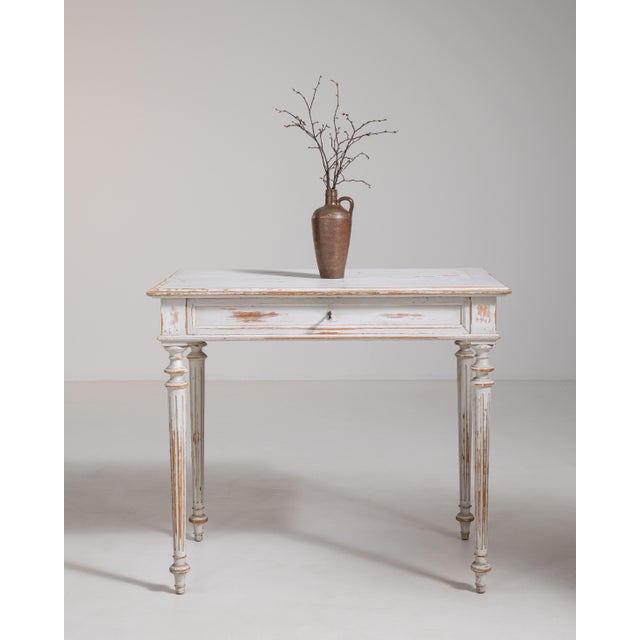 A delicate Louis XVI table featuring a white patinated finish that enhances its decorative appeal. The straight lines and...
