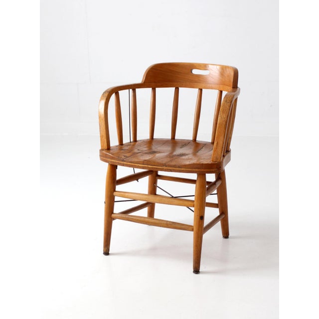 Vintage Early American captain's chair in warm oak, featuring a continuous curved arm, turned spindle back, sculpted crest...